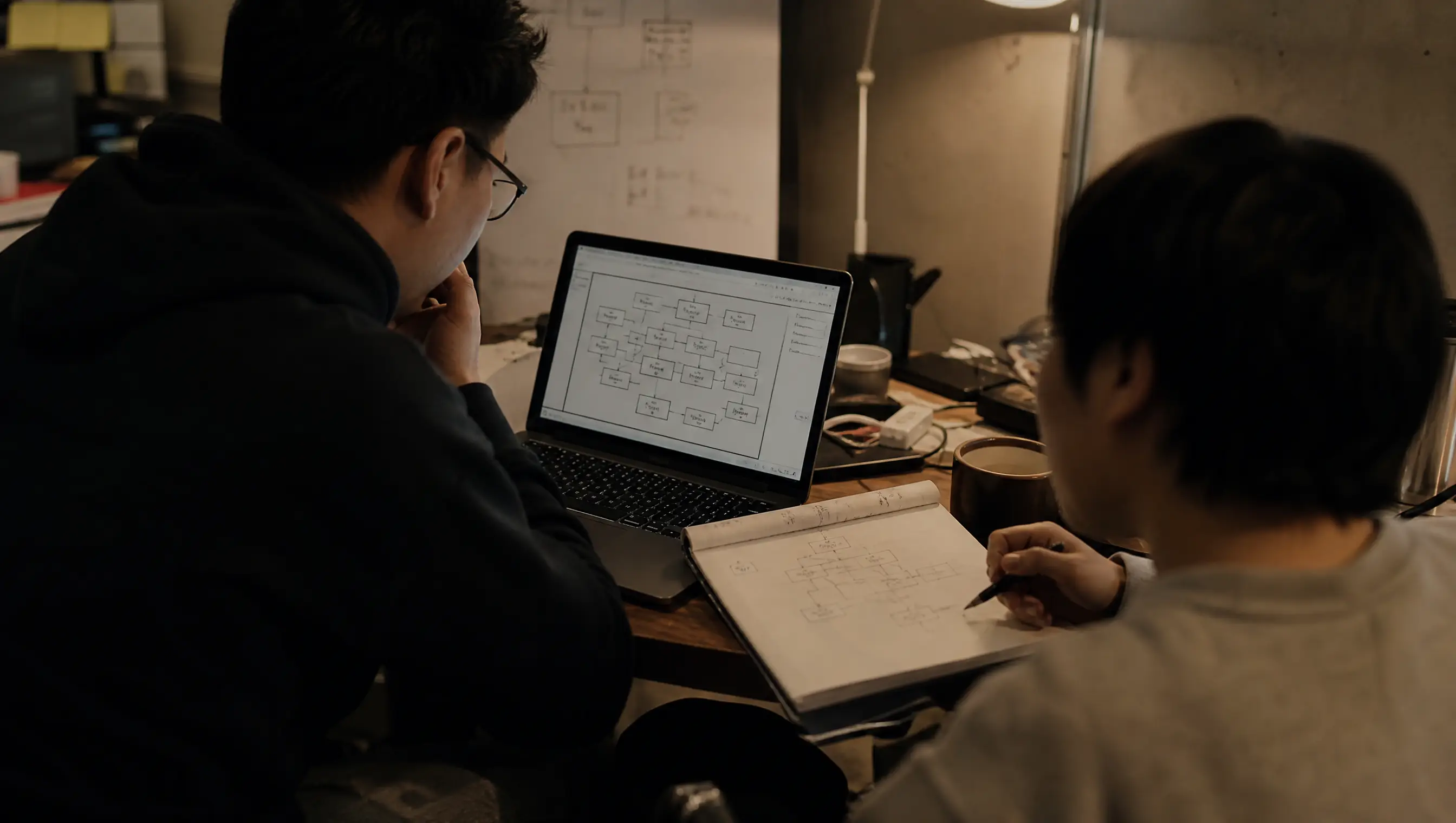 Two engineers reviewing an architecture diagram at a shared desk